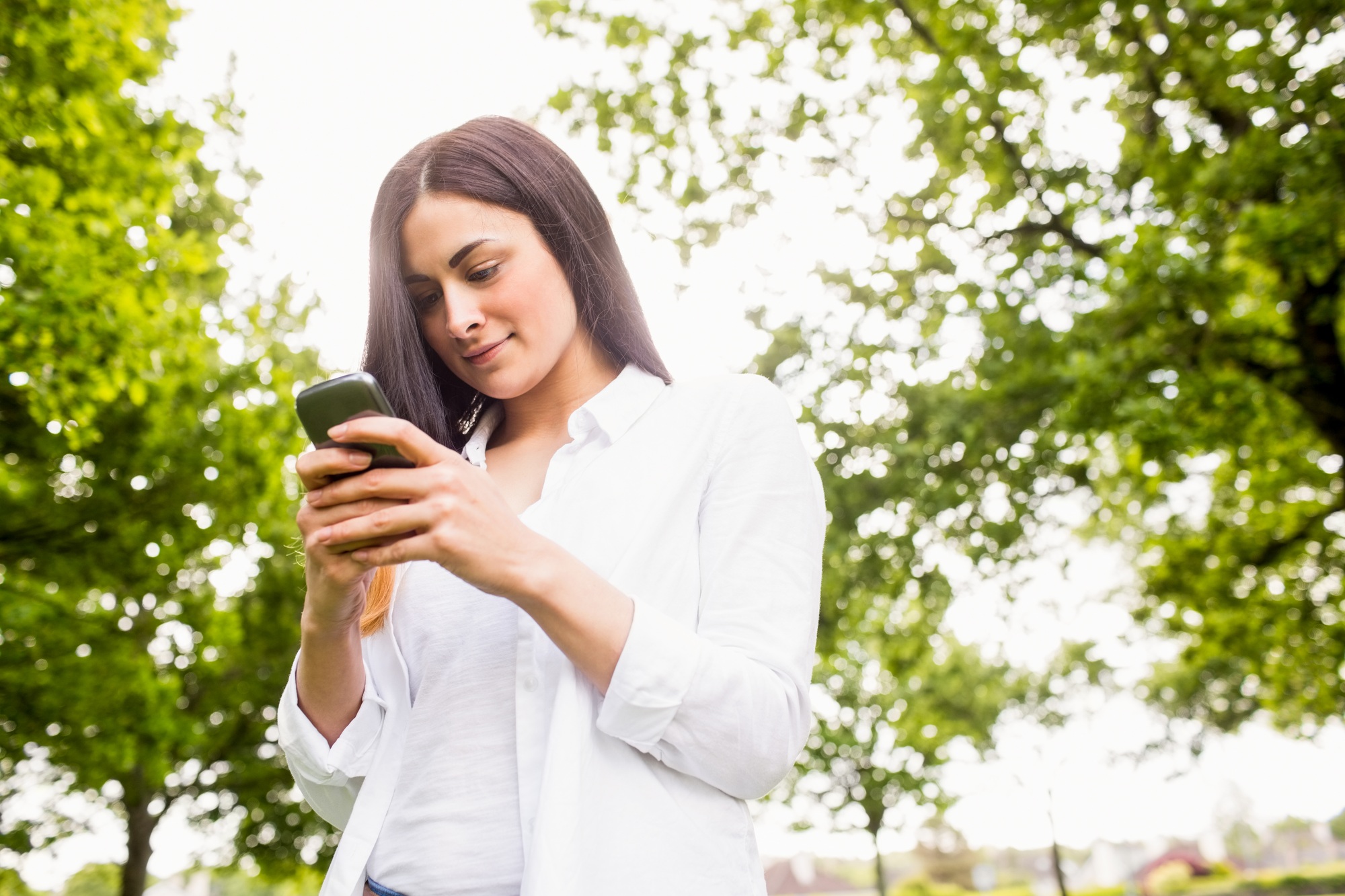 Beautiful brunette sending a text message on a sunny day