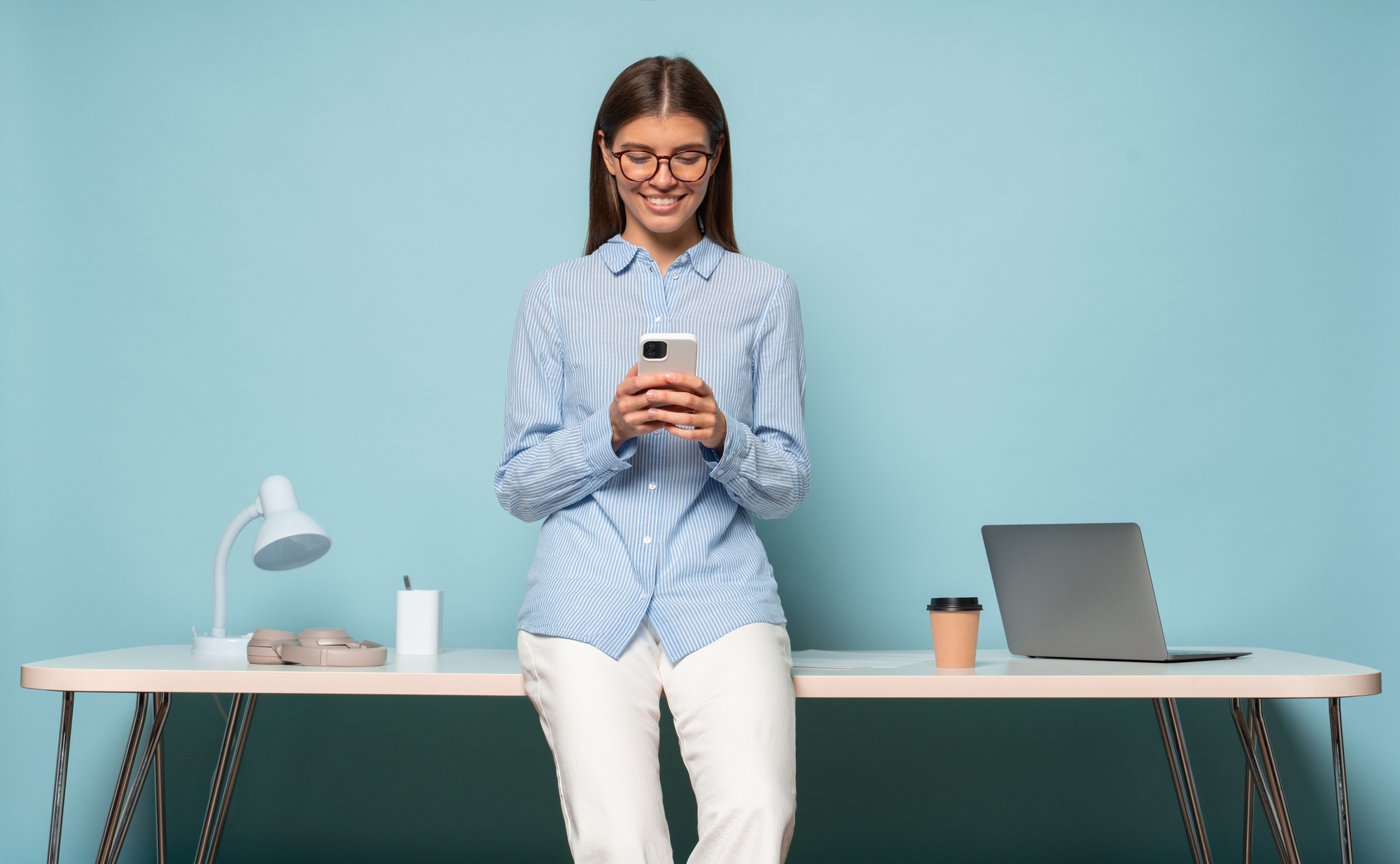 HR manager sitting on table over blue studio background checking messenger on phone