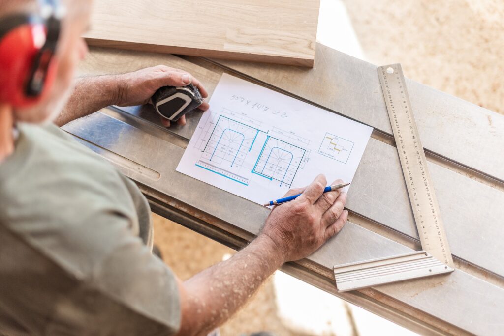 person drawing on wooden board with tape measure and ruler